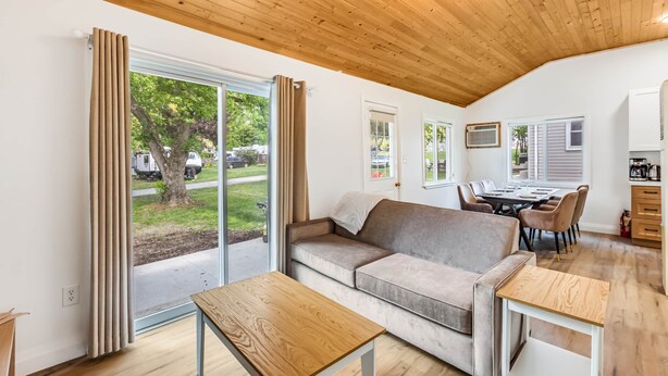 A modern living room with a wooden ceiling, a sofa, a table, and a view of the outdoors.