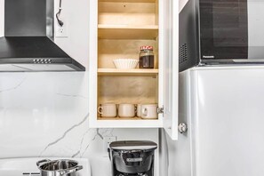 A kitchen with a microwave, a coffee maker, and a cabinet with mugs and a jar. - #7 Cottage - Peru (Lakeside) (Hamilton)