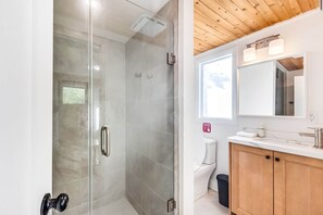 A modern bathroom with a glass shower enclosure, a white toilet, and a wooden vanity with a mirror. - #7 Cottage - Peru (Lakeside) (Hamilton)