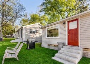 Une maison mobile avec une porte rouge, un barbecue et une chaise blanche dans la cour.