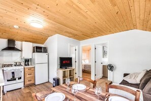 A compact kitchen with modern appliances, a dining area with a wooden table set for four, and a cozy living space with a couch and a fan. - #1 Cottage - South Africa (Hamilton)