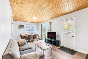 A modern living room with a wooden ceiling, a sofa, a dining table, and a TV displaying 'NETFLIX'. - #5 Cottage - Sri Lanka (Hamilton)