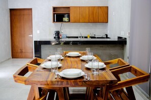 Un comedor con una mesa de madera dispuesta para seis, una cocina al fondo y una puerta de madera.