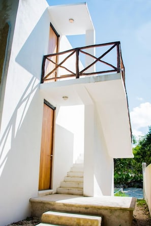 Un edificio moderno con fachada blanca, puerta de madera y una escalera que lleva a un balcón con barandilla de metal.