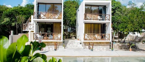 A modern two-story building with balconies, a pool, and a clear sky.