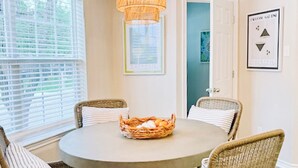 Un coin repas avec une table ronde, des chaises en osier, un lustre et un panier de pain posé sur la table.