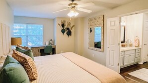 Une chambre à coucher avec un grand lit, un bureau, une chaise, une armoire et un ventilateur de plafond.