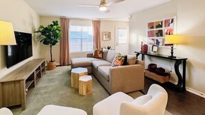 Un salon comprenant un canapé, deux fauteuils, une table basse, un téléviseur, un ventilateur de plafond, une plante et une bibliothèque.