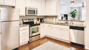 Une cuisine moderne avec des meubles blancs, des appareils en acier inoxydable, un four à micro-ondes, une cuisinière et un lave-vaisselle.