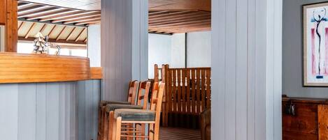 A modern interior with a wooden ceiling, a bar area, and a dining space with wooden chairs and a striped floor.
