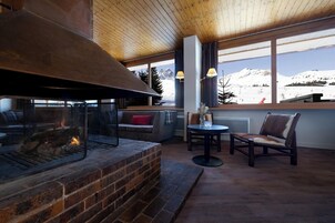 Un intérieur chaleureux avec une cheminée, un coin salon et une vue sur une montagne enneigée.