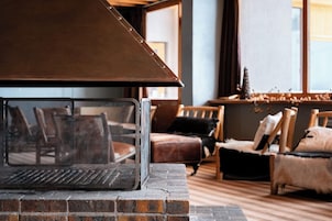 Uma lareira com proteção de metal, base de tijolos e um banco de madeira em um quarto com piso de madeira e janela.
