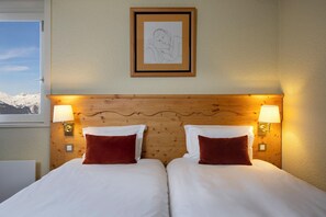 A double bed with two pillows, a wooden headboard, two wall-mounted lamps, and a framed drawing on the wall. - Crystal Hôtel Courchevel (Les Allues)