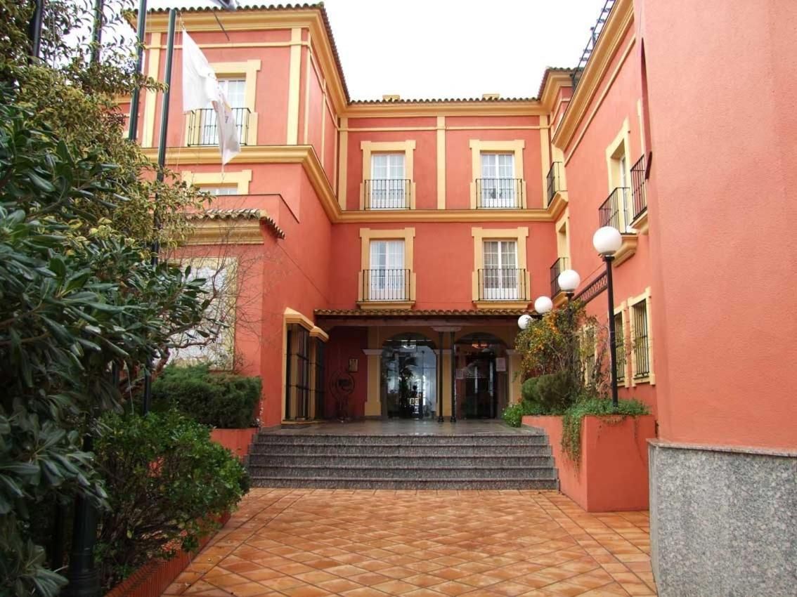 Un edificio con fachada roja, una entrada central con escalones y un patio adoquinado.