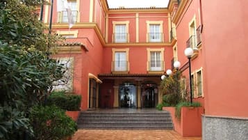 Un edificio con fachada roja, una entrada central con escalones y un patio adoquinado.