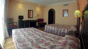 Habitación de hotel con dos camas, un escritorio, una silla, un televisor y una lámpara.
