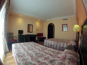 Habitación de hotel con dos camas, un escritorio, una silla, un televisor y una lámpara.