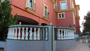 Un edificio con fachada rosa, balcones con barandillas negras y una cerca de azulejos con balaustres blancos.