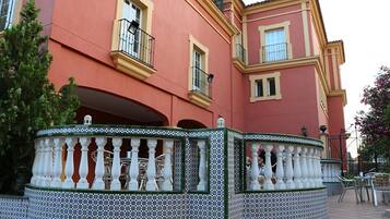Un edificio con fachada rosa, balcones con barandillas negras y una cerca de azulejos con balaustres blancos.