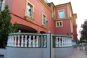 Un edificio con fachada rosa, balcones con barandillas negras y una cerca de azulejos con balaustres blancos.