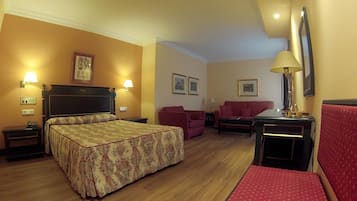 Una habitación de hotel con una cama, un sillón rojo, un sofá, una mesita y una lámpara.