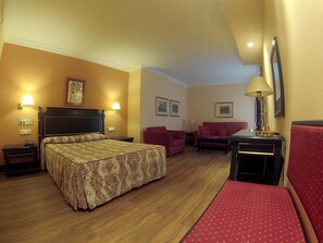 Una habitación de hotel con una cama, un sillón rojo, un sofá, una mesita y una lámpara.