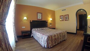 Habitación de hotel con cama, mesitas de noche, lámparas de pared y cuadros enmarcados.