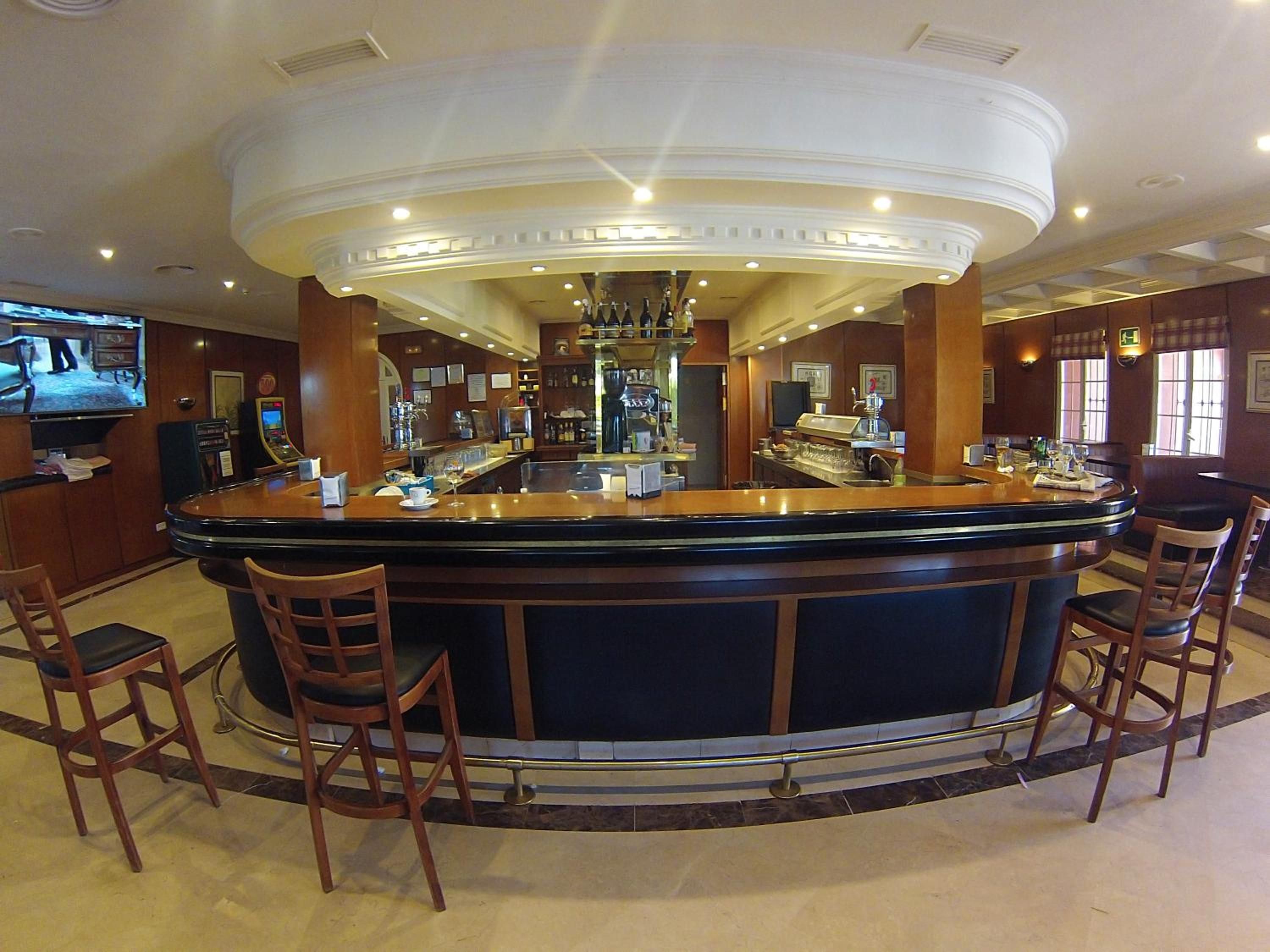 Una zona de bar con mostrador curvo, taburetes y una pantalla de televisión.