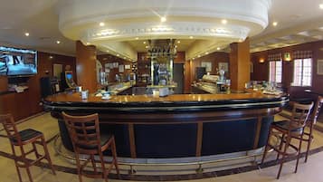 Una zona de bar con mostrador curvo, taburetes y una pantalla de televisión.