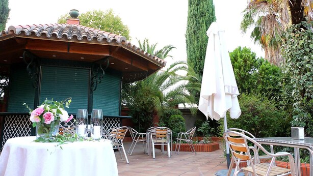 Un patio al aire libre con un área de estar cubierta, una mesa con un centro de mesa floral y una palmera alta al fondo.