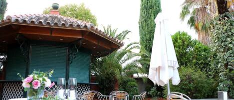 An outdoor patio with a covered seating area, a table with a floral centerpiece, and a tall palm tree in the background.