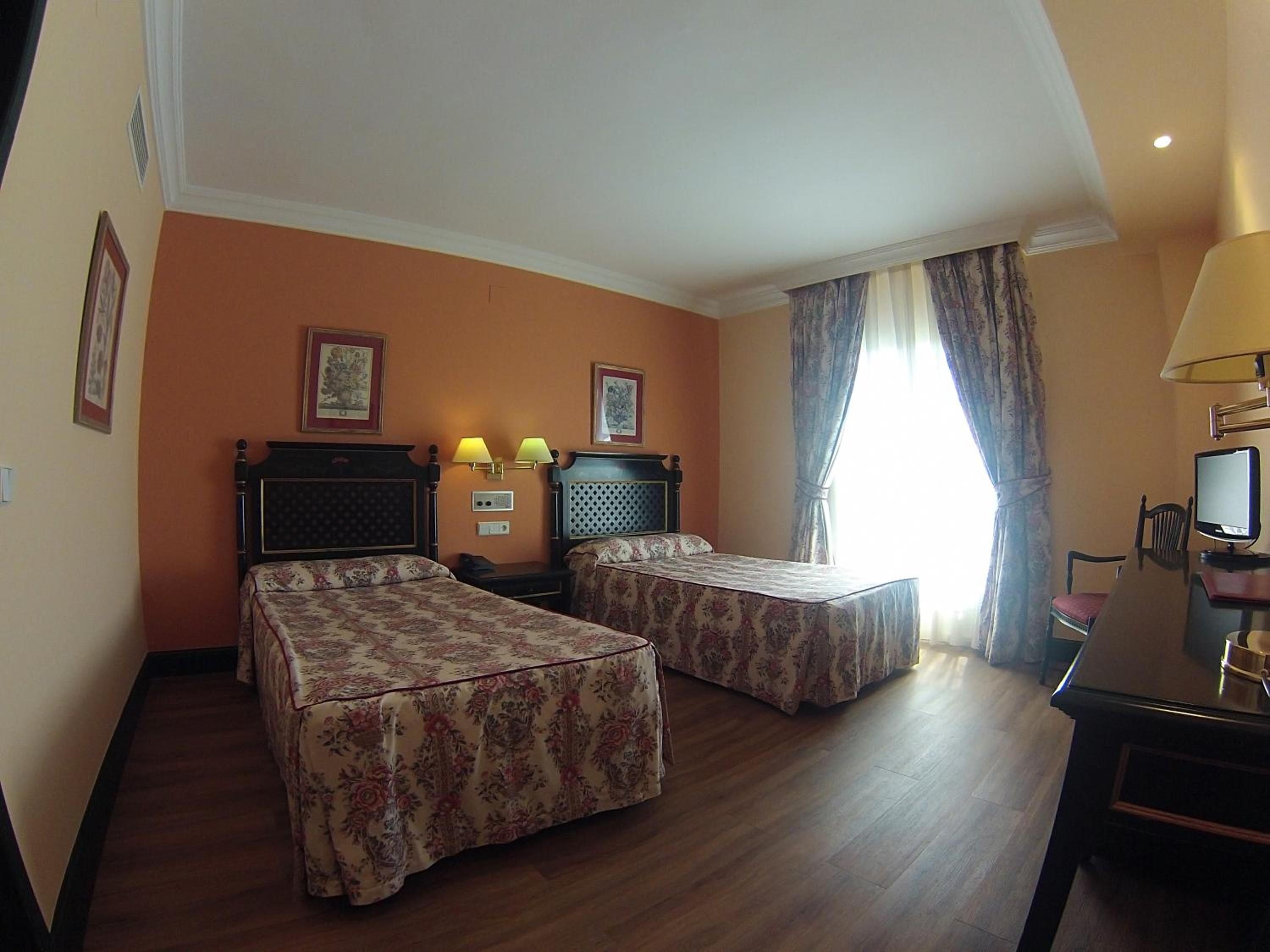 Una habitación de hotel con dos camas, un escritorio con ordenador y una ventana con cortinas.