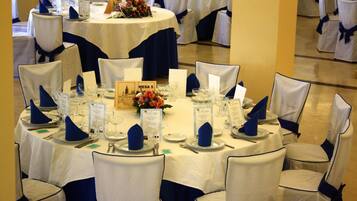 Un salón de banquetes con mesas redondas, manteles blancos y sillas adornadas con cintas azules.