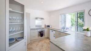 A modern kitchen with built-in appliances, a large window, and a view of greenery. - Snells Beach Family Retreat — Walk to Shops & Beach (Snells Beach)