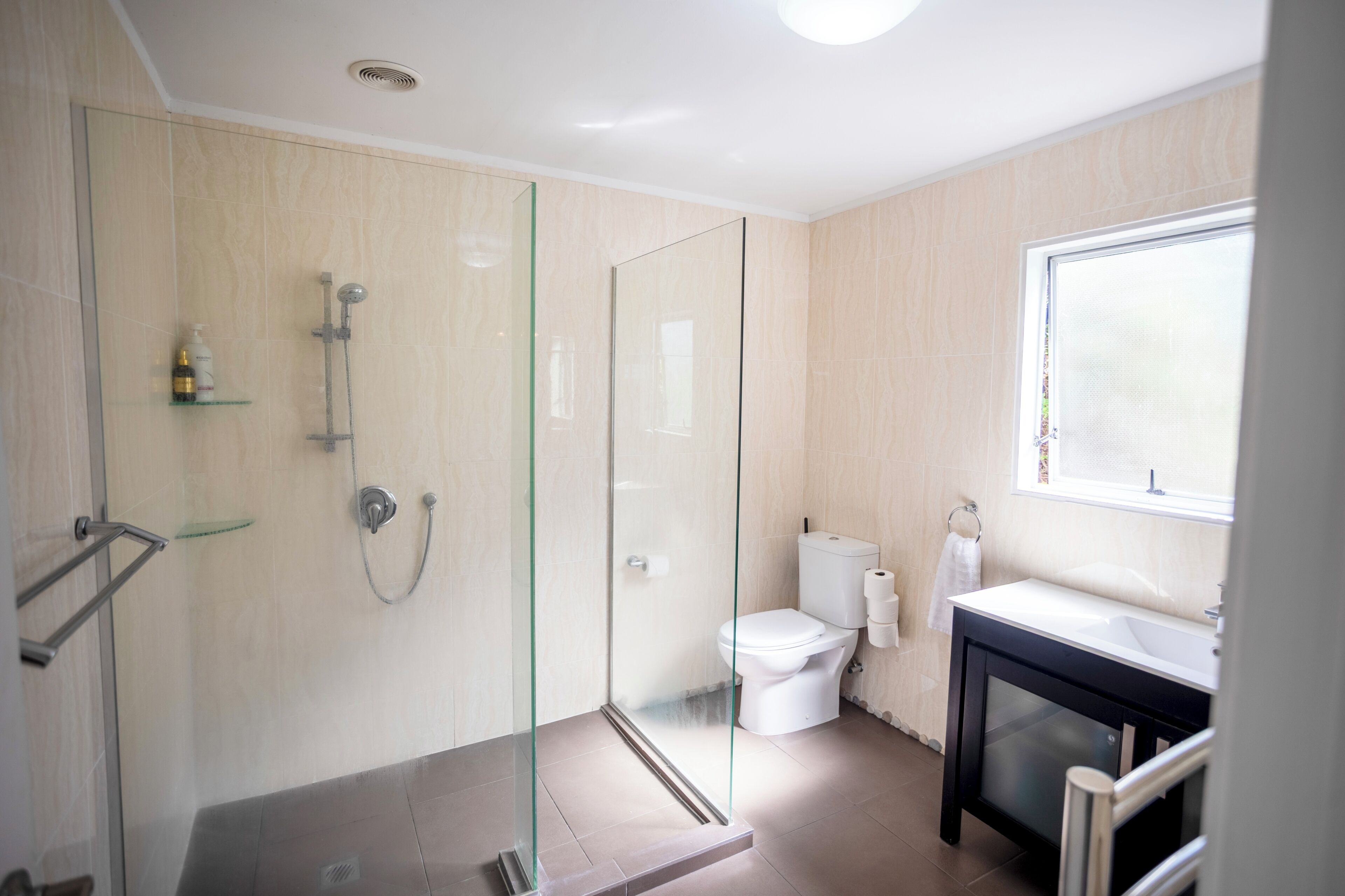 A modern bathroom with a glass-enclosed shower, a toilet, and a sink with a window above.