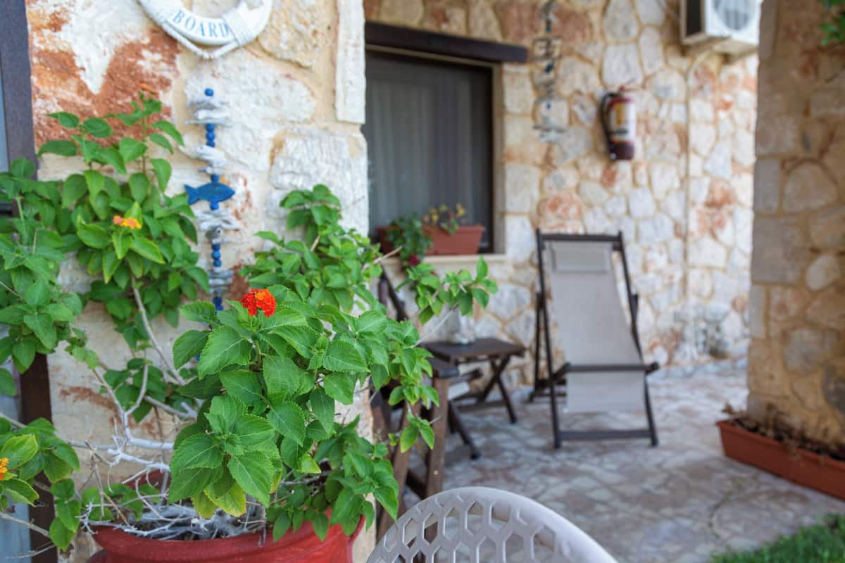 Un bâtiment en pierre, avec un pot de fleurs rouge et une chaise blanche au premier plan.