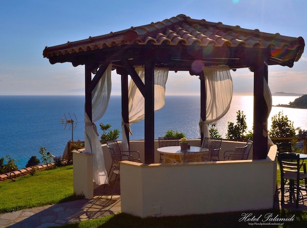 A gazebo with a tiled roof and white curtains, overlooking a scenic ocean view.