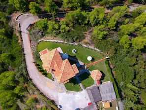 An aerial view of a property with a winding driveway, a fenced area, and a building with a tiled roof.