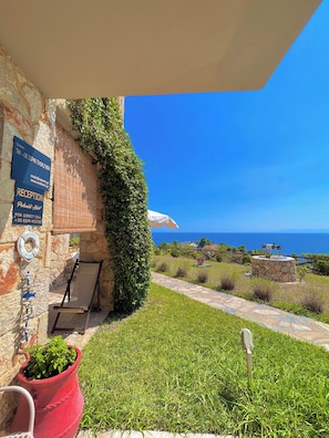 A reception area with a stone wall, a signboard, a potted plant, and a view of the sea. - Palamidi Boutique Apartments (Kassandra)