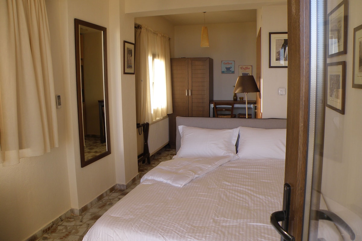 A hotel room with a bed, a desk, a chair, and a radiator.
