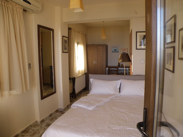A hotel room with a bed, a desk, a chair, and a radiator. - Palamidi Boutique Apartments (Kassandra)