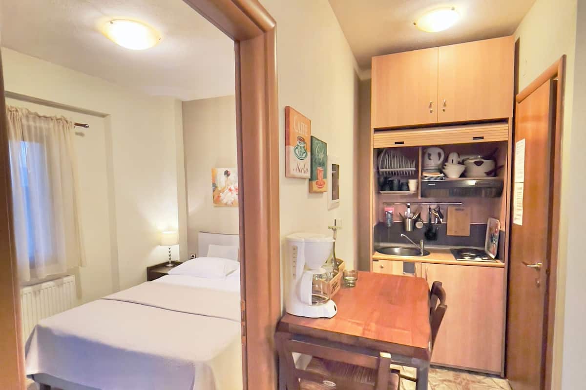 Une chambre d’hôtel avec un lit, une petite table avec des chaises, un coin cuisine et une salle de bain visible à travers une porte ouverte.