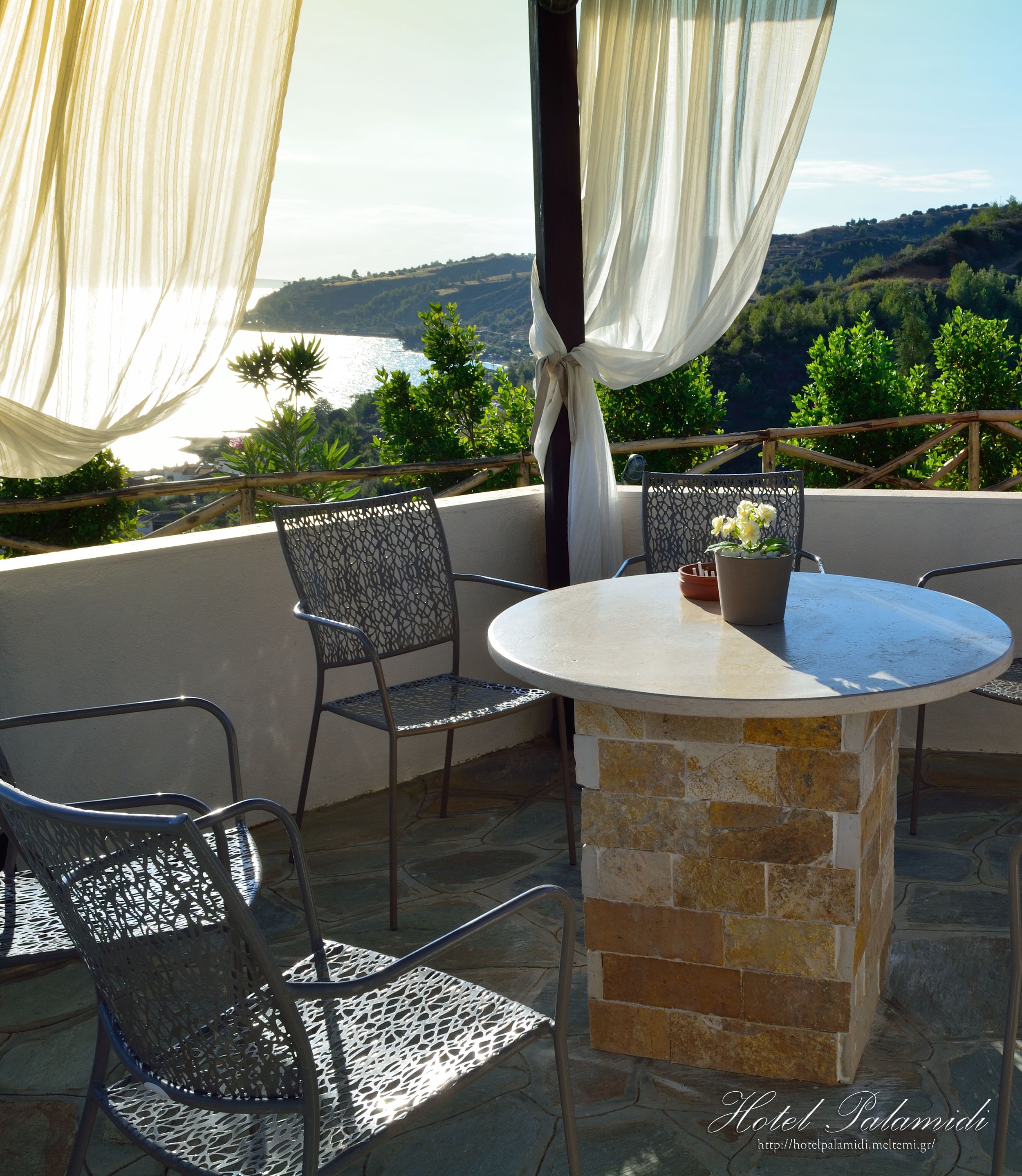 A terrace with a round table and metal chairs, overlooking a scenic landscape.