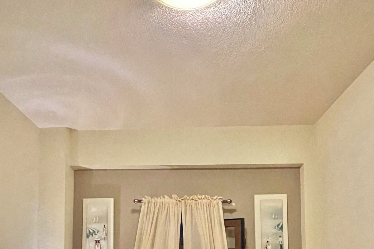 Una habitación de hotel con cama, dos mesitas de noche, una ventana con cortinas y decoración en la pared.