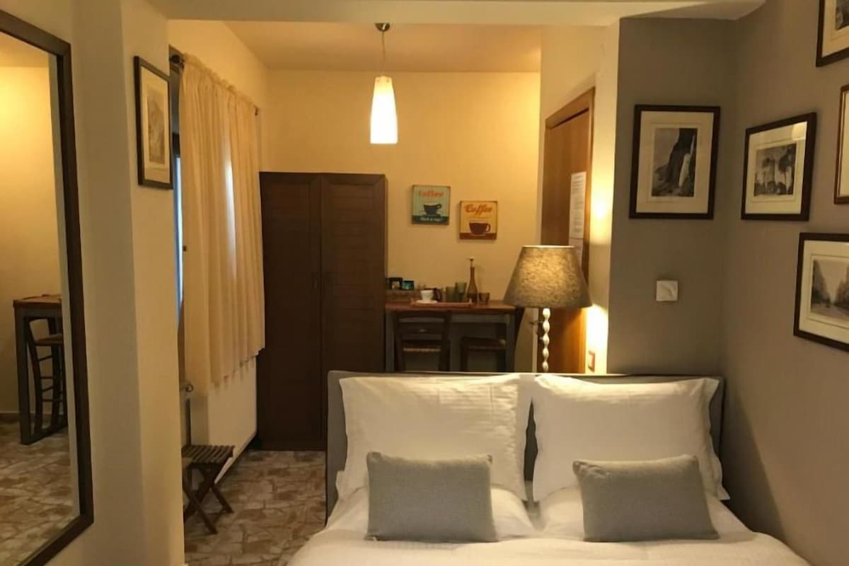A hotel room with a bed, a desk, a lamp, and framed pictures on the wall.