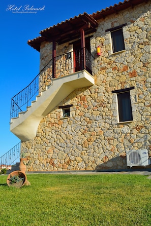 A stone building with a staircase leading to a balcony, a small window, and an air conditioning unit. - Palamidi Boutique Apartments (Kassandra)