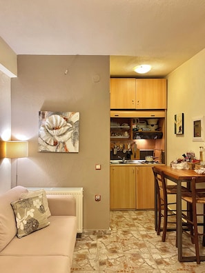A compact living space with a kitchenette, a dining area, and a sofa with floral cushions. - Palamidi Boutique Apartments (Kassandra)