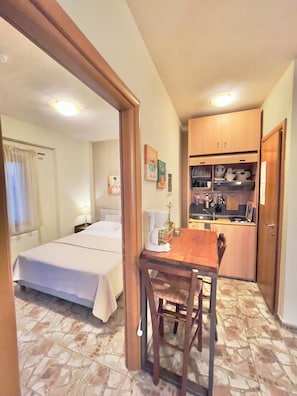 A hotel room with a bed, a small table with chairs, a kitchenette, and a bathroom visible through an open door.
