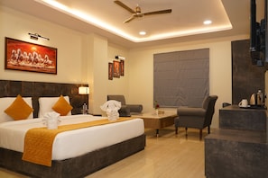 A hotel room with a large bed, a desk, a chair, and a ceiling fan. - Shrigo Hotel Banaras - Varanasi (Varanasi)