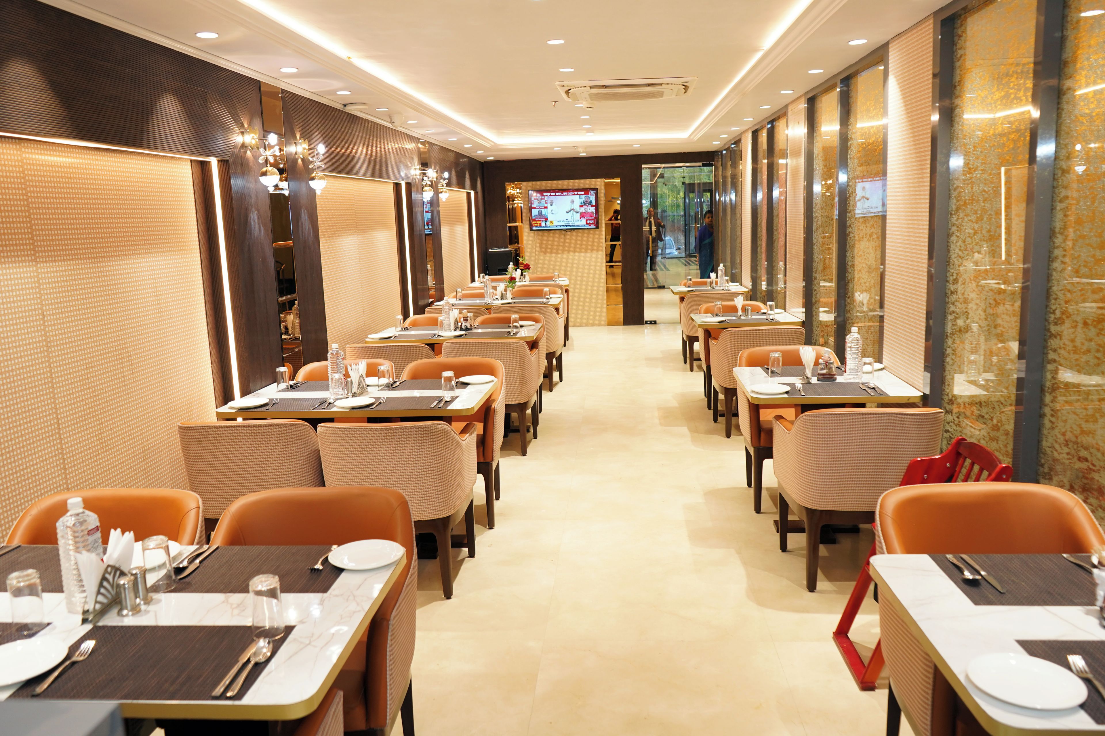 A restaurant with multiple tables and chairs, a television screen, and a tiled floor.